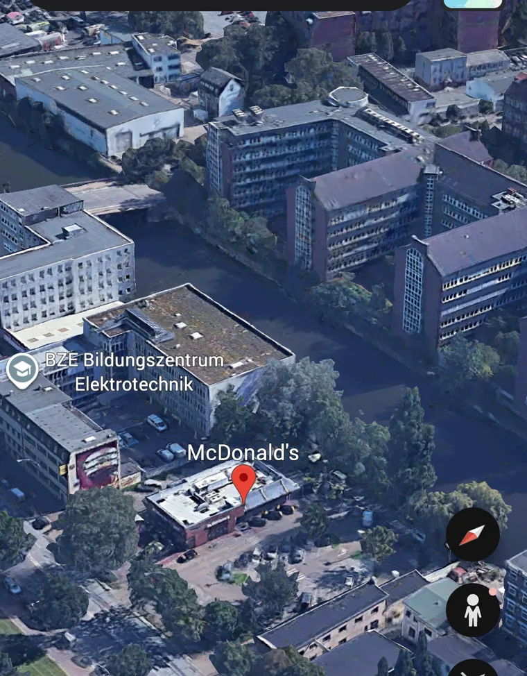 Zugeschnittener Google-Earth-Screenshot in 3D-Schrägansicht mit einem roten Standort-Pin auf einem Gebäude, ohne App-Bedienelemente