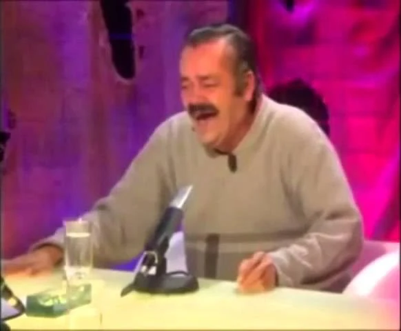 Unscharfes Standbild aus einem alten Fernsehclip: ein lachender Mann mit Schnurrbart an einem Studiotisch